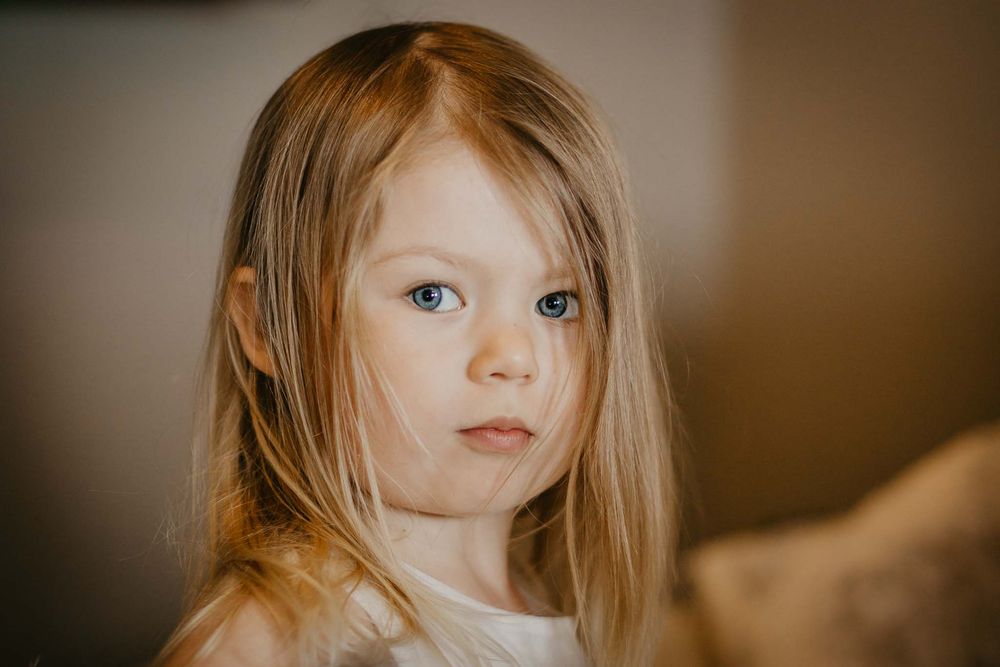 Portrait of a young girl with long blonde hair and blue eyes wearing a white top.