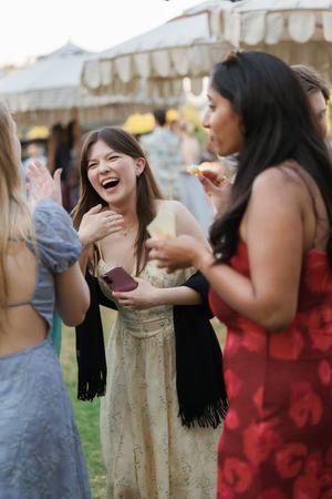 Women laughing and socializing at an outdoor summer party, wearing elegant dresses in a festive garden setting.