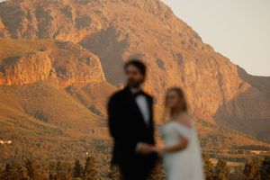 Blurred couple in wedding attire with dramatic sunlit mountain backdrop at golden hour.