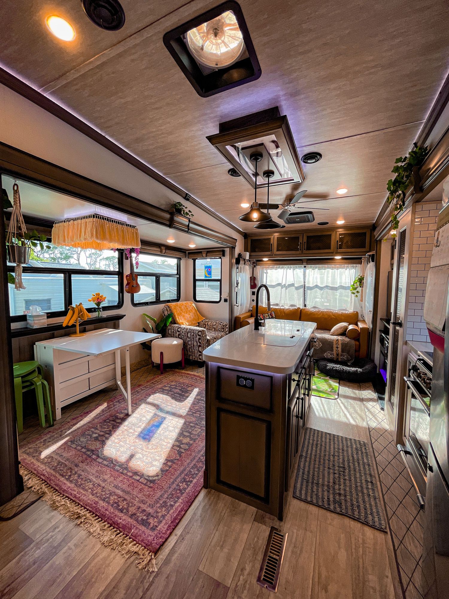 Bright and cozy RV interior with wood floors, kitchen island, dining area, and colorful rugs.