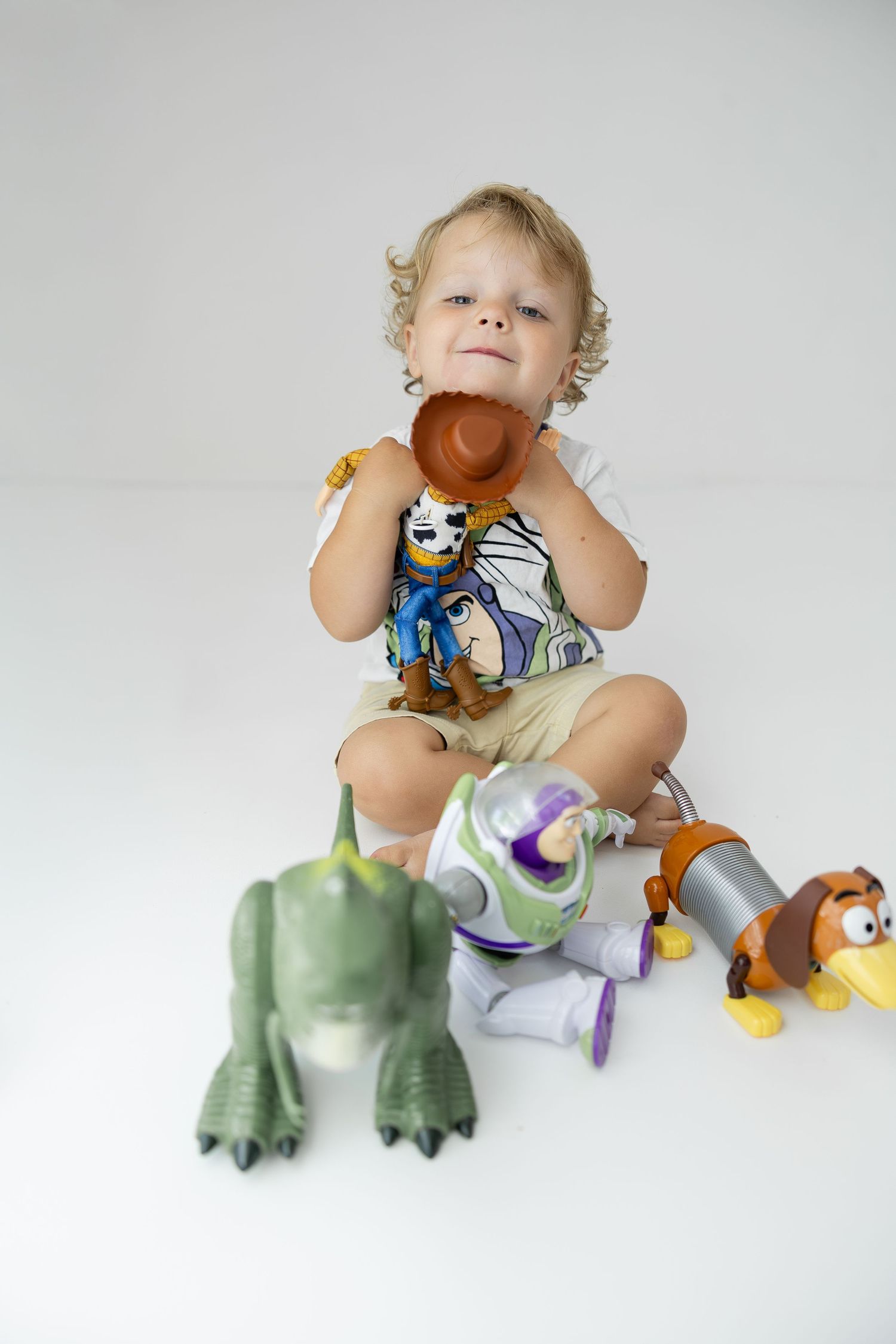 Toddler boy playing with Toy Story character figures including Woody, Buzz, Rex, and Slinky Dog.
