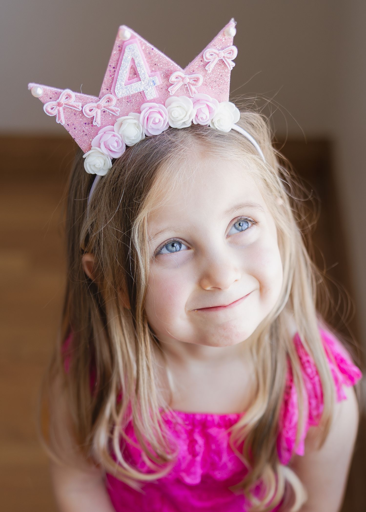 Adorable young girl with blue eyes wearing pink number 4 birthday crown with white roses on headband.