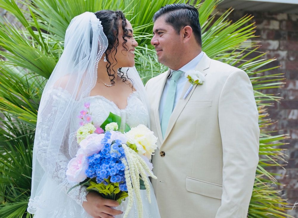 Bride and groom gazing at each other, bride holding blue hydrangea bouquet, groom in ivory suit with mint tie.