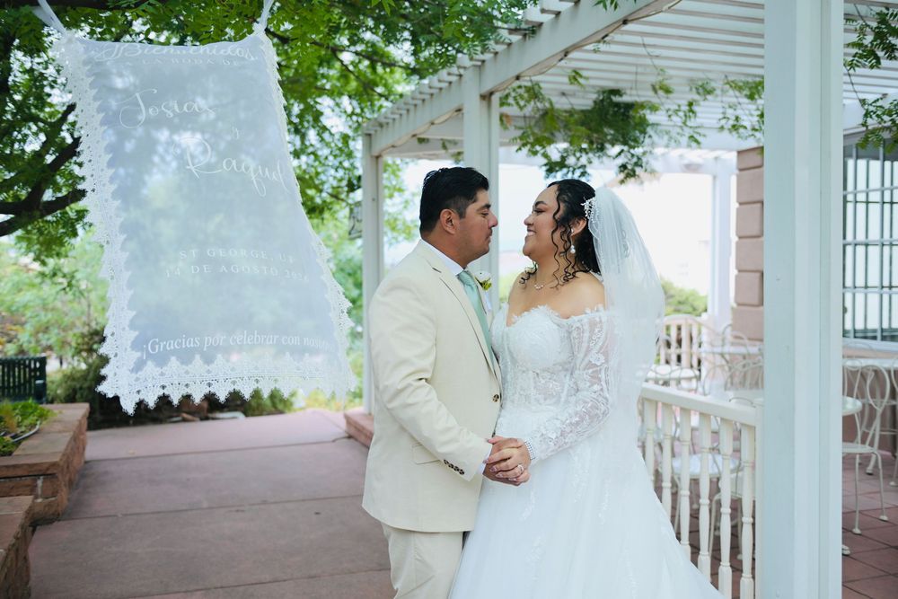 A bride and groom share a romantic moment under a white gazebo, surrounded by lush greenery on their wedding day.