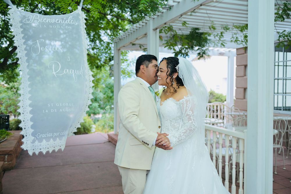 Bride and groom share a kiss under a pergola at an outdoor wedding ceremony with decorative banners.