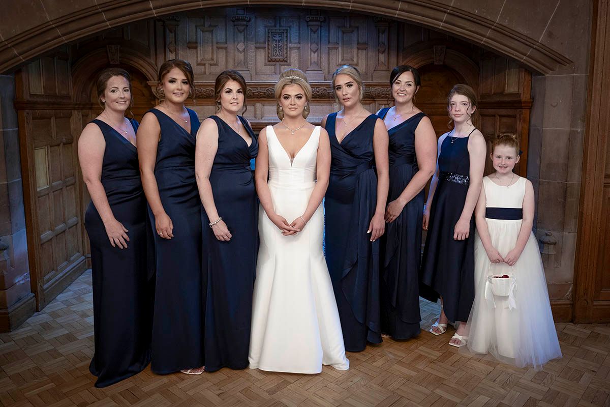 Bride in white gown poses with six bridesmaids in navy blue dresses and flower girl in white dress in elegant venue Dalston Hall- Carlisle
