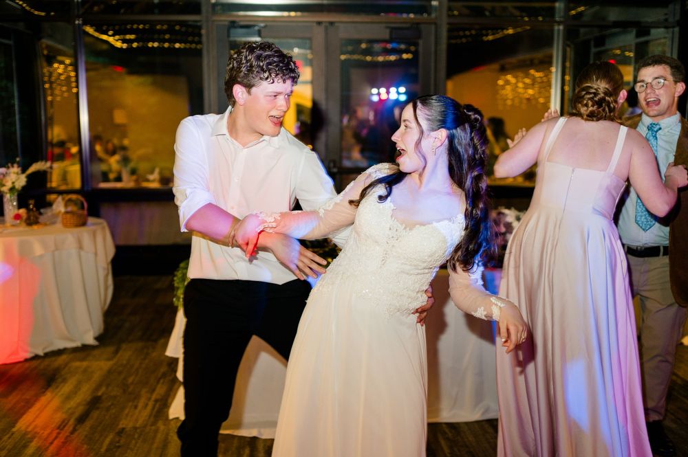 Bride and groom dancing joyfully at wedding reception with guests in background.