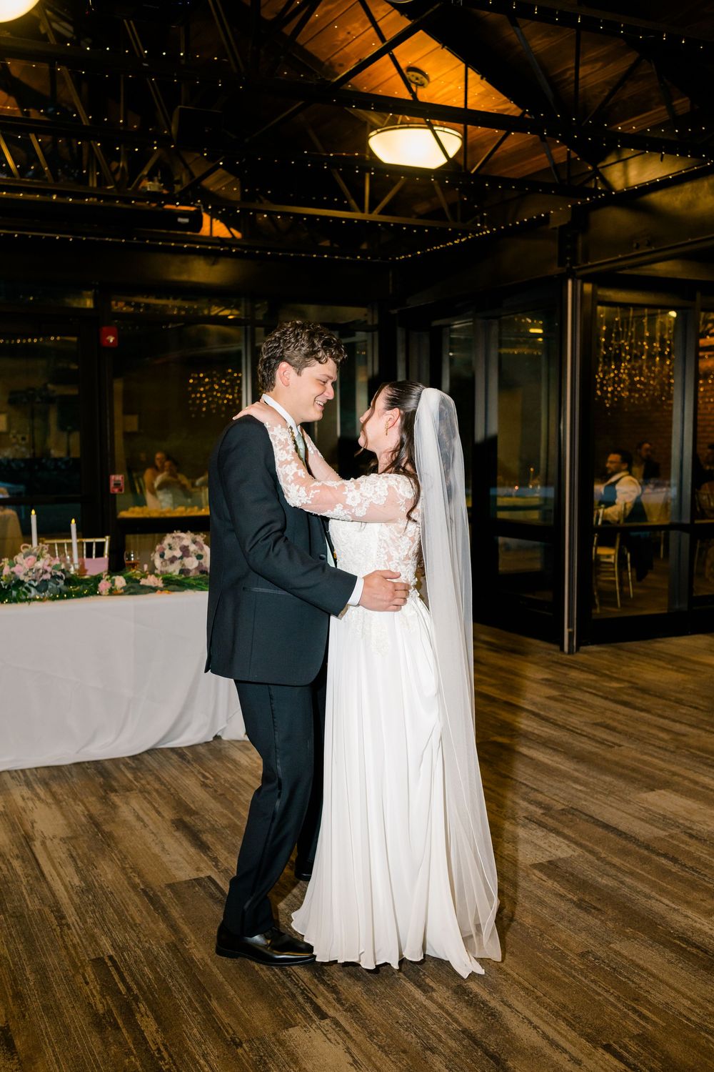 Bride and groom share their first dance on a wooden dance floor at an elegant indoor wedding reception venue.