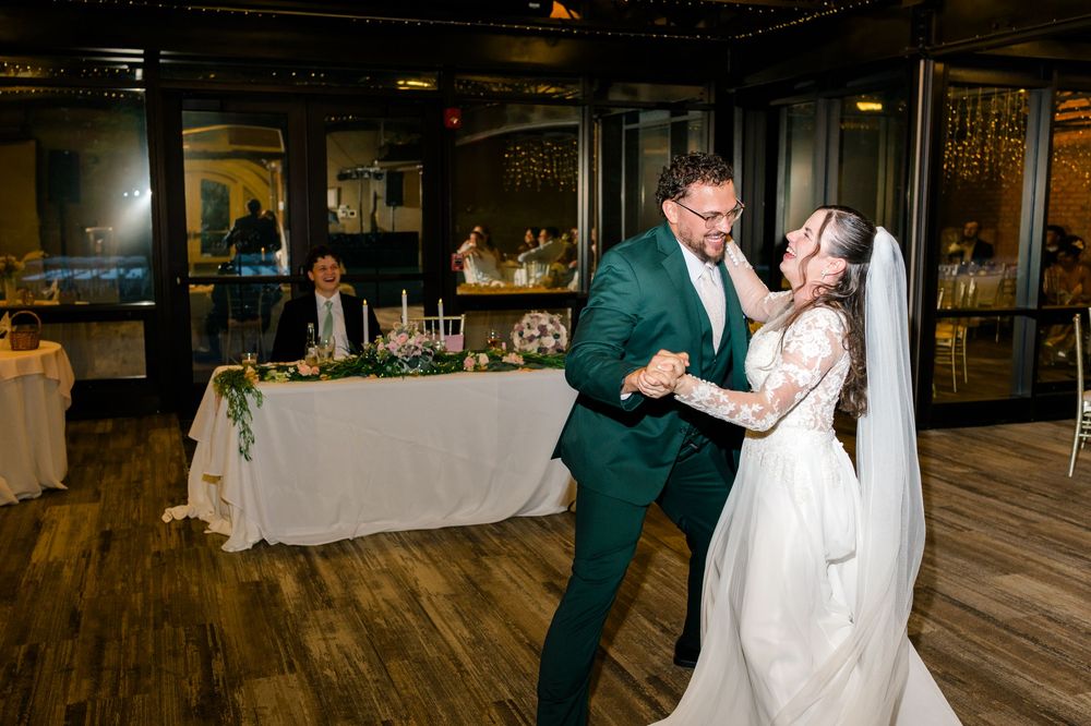 Bride and groom share their first dance at elegant indoor wedding reception with greenery-adorned head table.