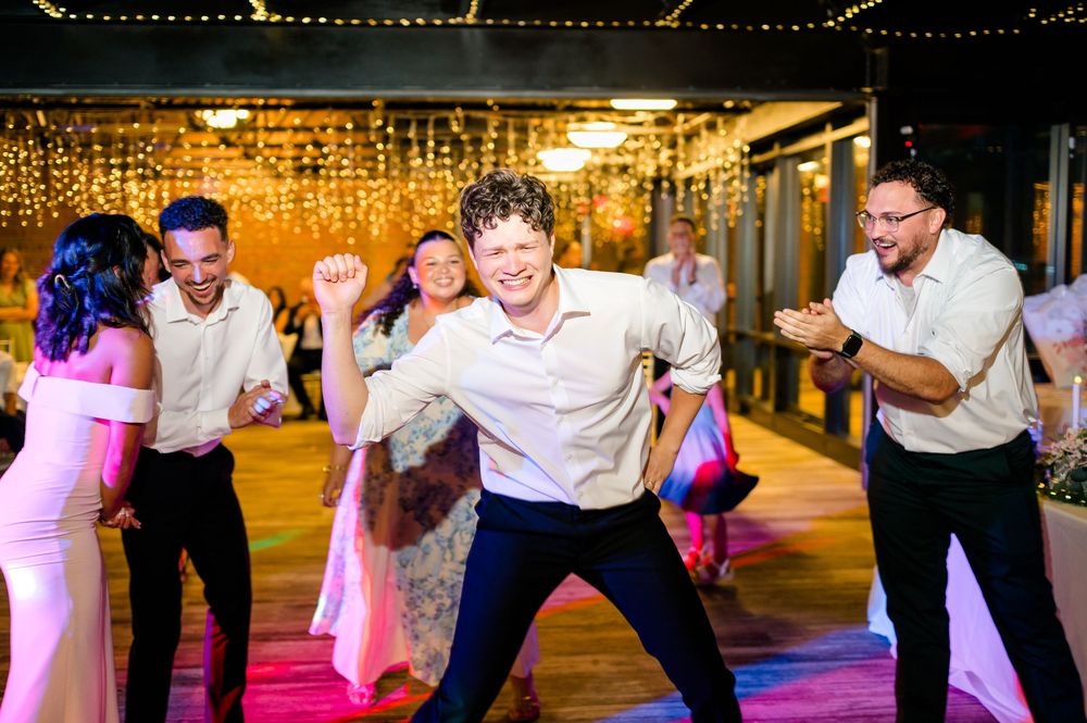 Guests dancing joyfully at a wedding reception with string lights glowing in the background.