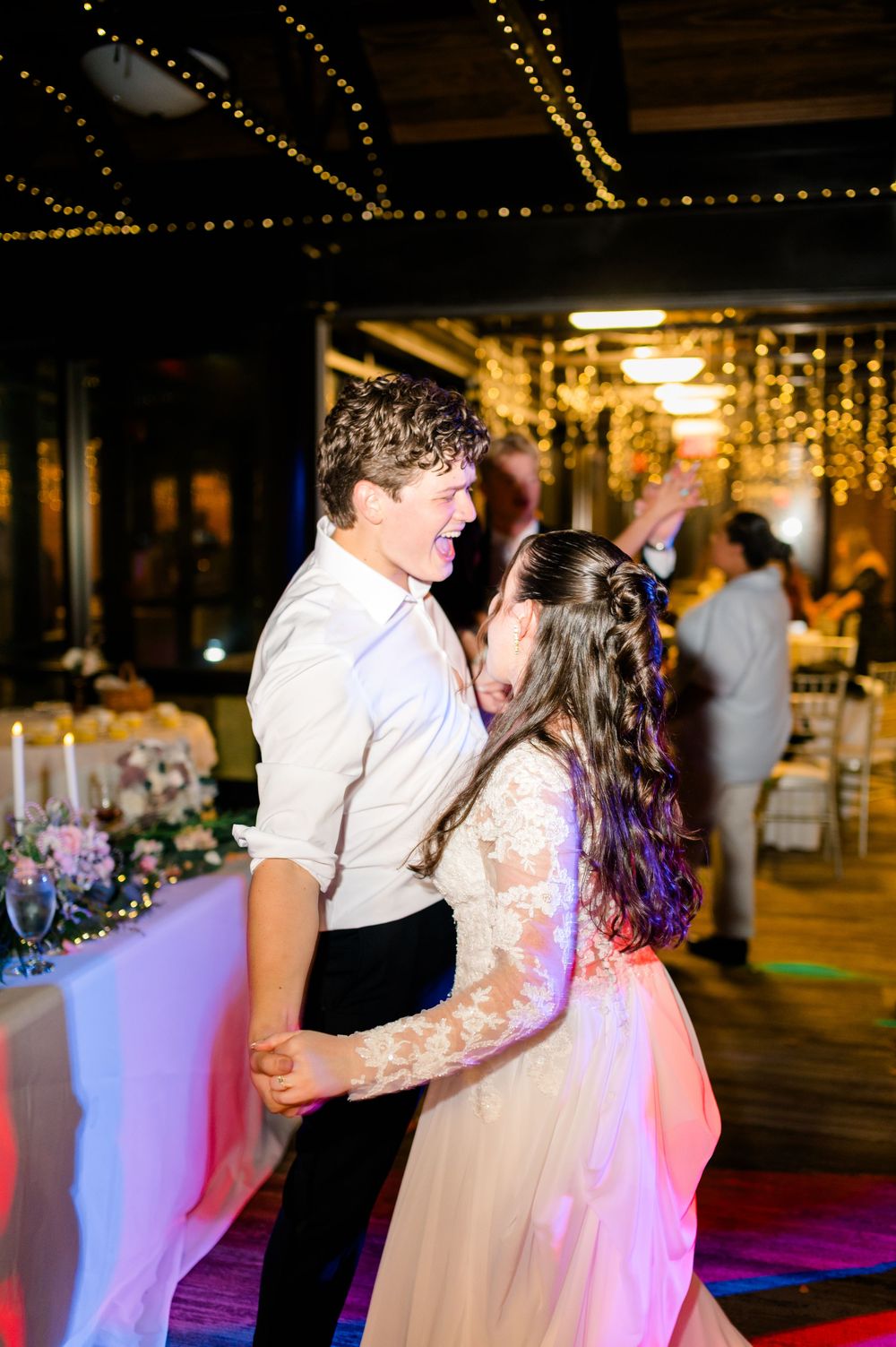 Couple sharing a joyful first dance at a wedding reception with fairy lights glowing in the background.
