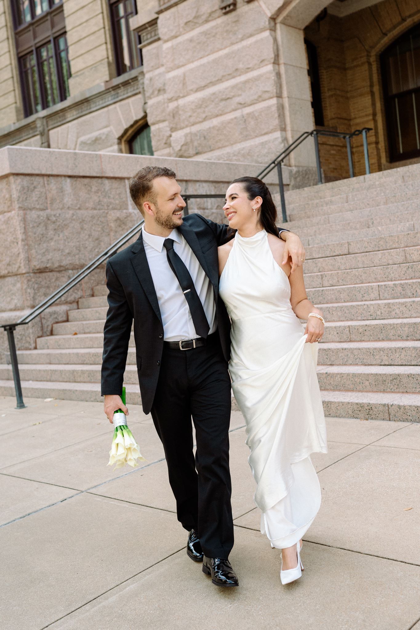 Bride and groom joyfully walking away from the historic 1910 Courthouse.