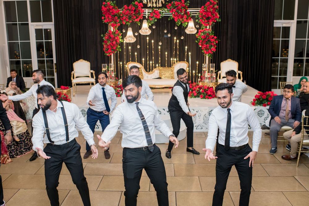 Groomsmen in white shirts and suspenders performing a coordinated dance at an Indian wedding reception.
