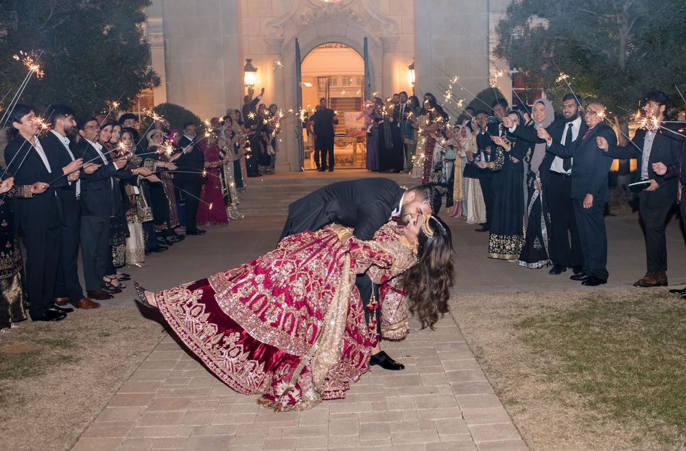 Bride in red lehenga and groom share a romantic dip during sparkler send-off at Indian wedding.