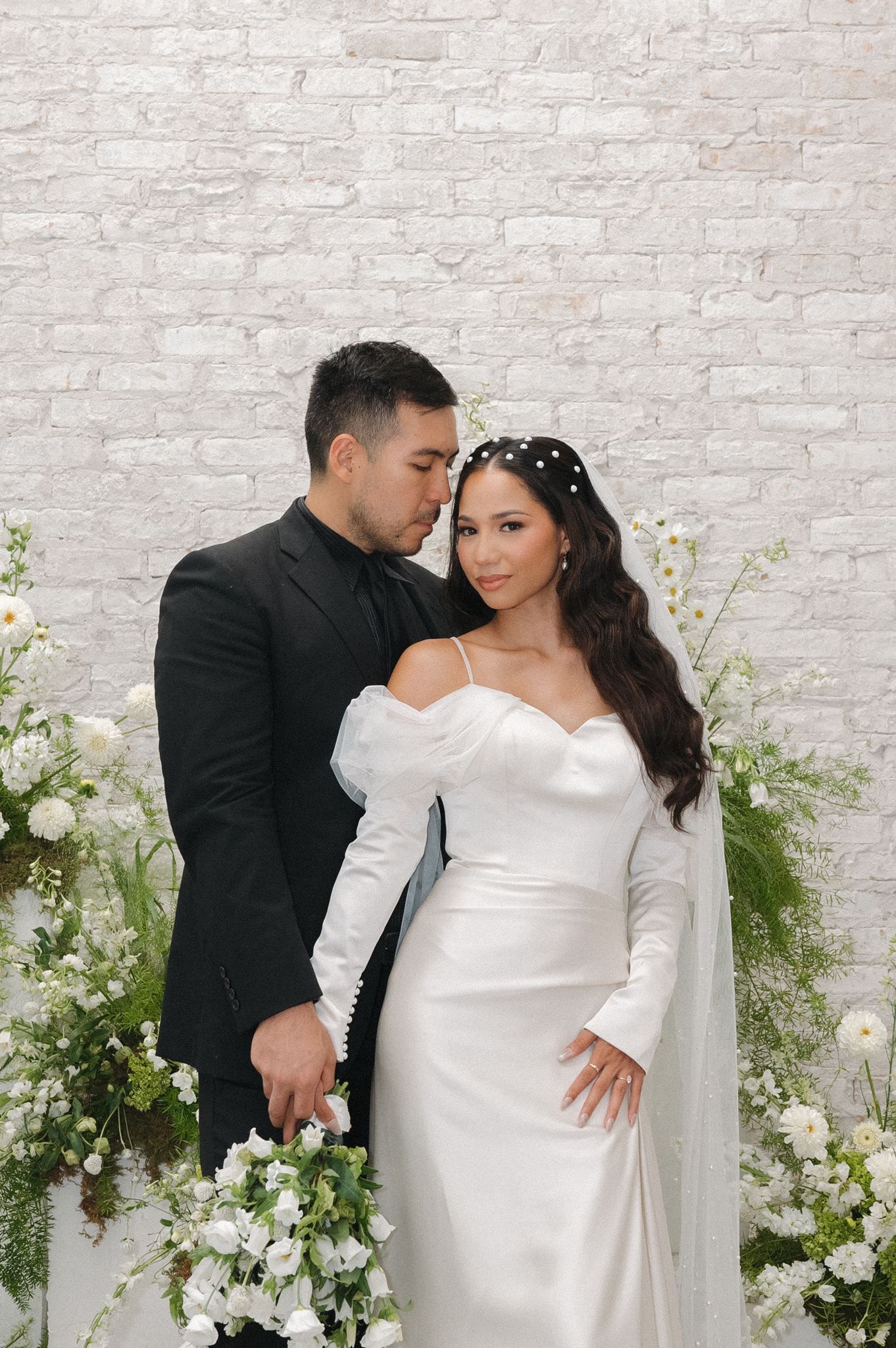 Bride and groom pose in front of white floral arrangements at the Oak Atelier in Conroe, Texas.