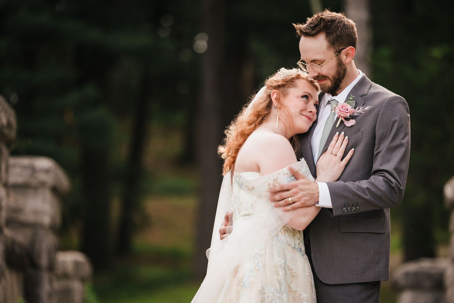 Bride resting her head on the groom's chest in a warm embrace, weathered stone pillars visible beside them.