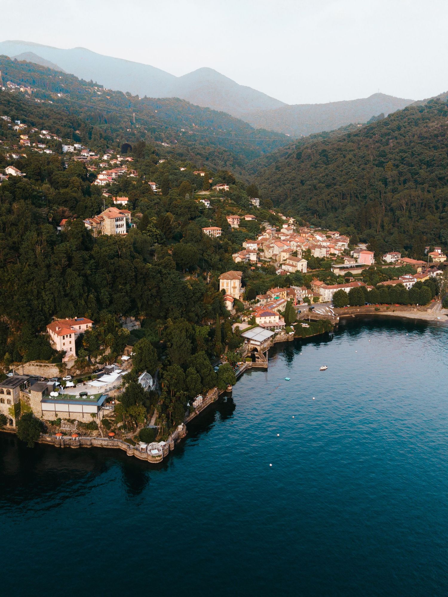 Aerial view of a picturesque Italian coastal village nestled among lush green hills beside calm blue Mediterranean waters.