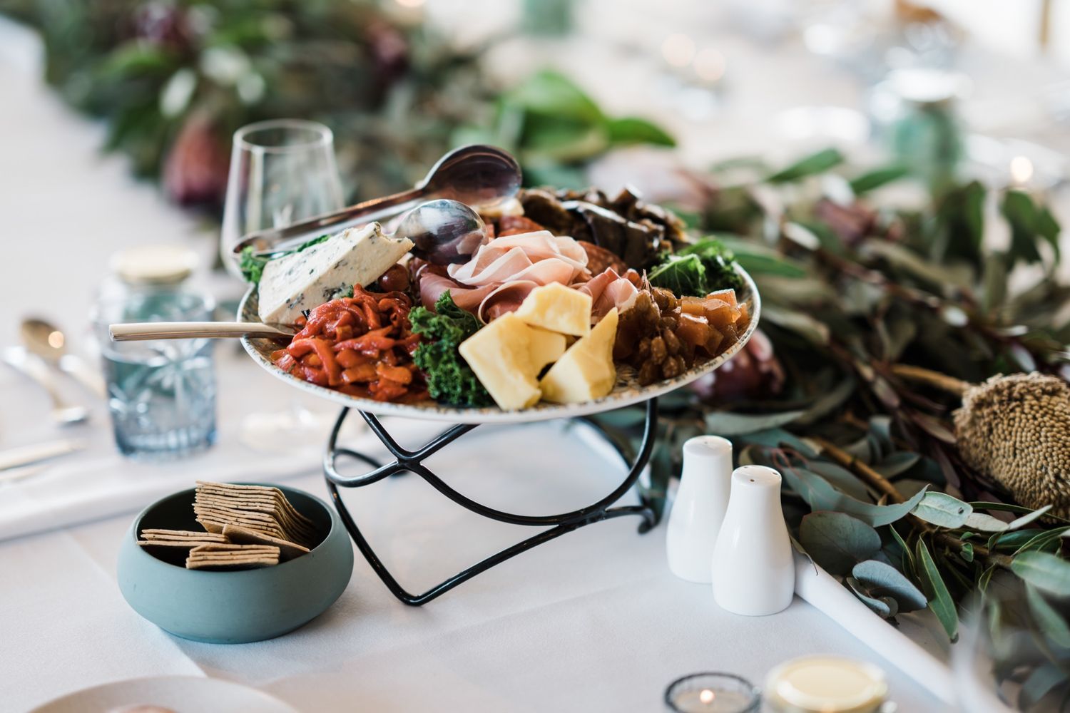 Elegant charcuterie board with cheese, meats, and garnishes on a decorated wedding reception table.