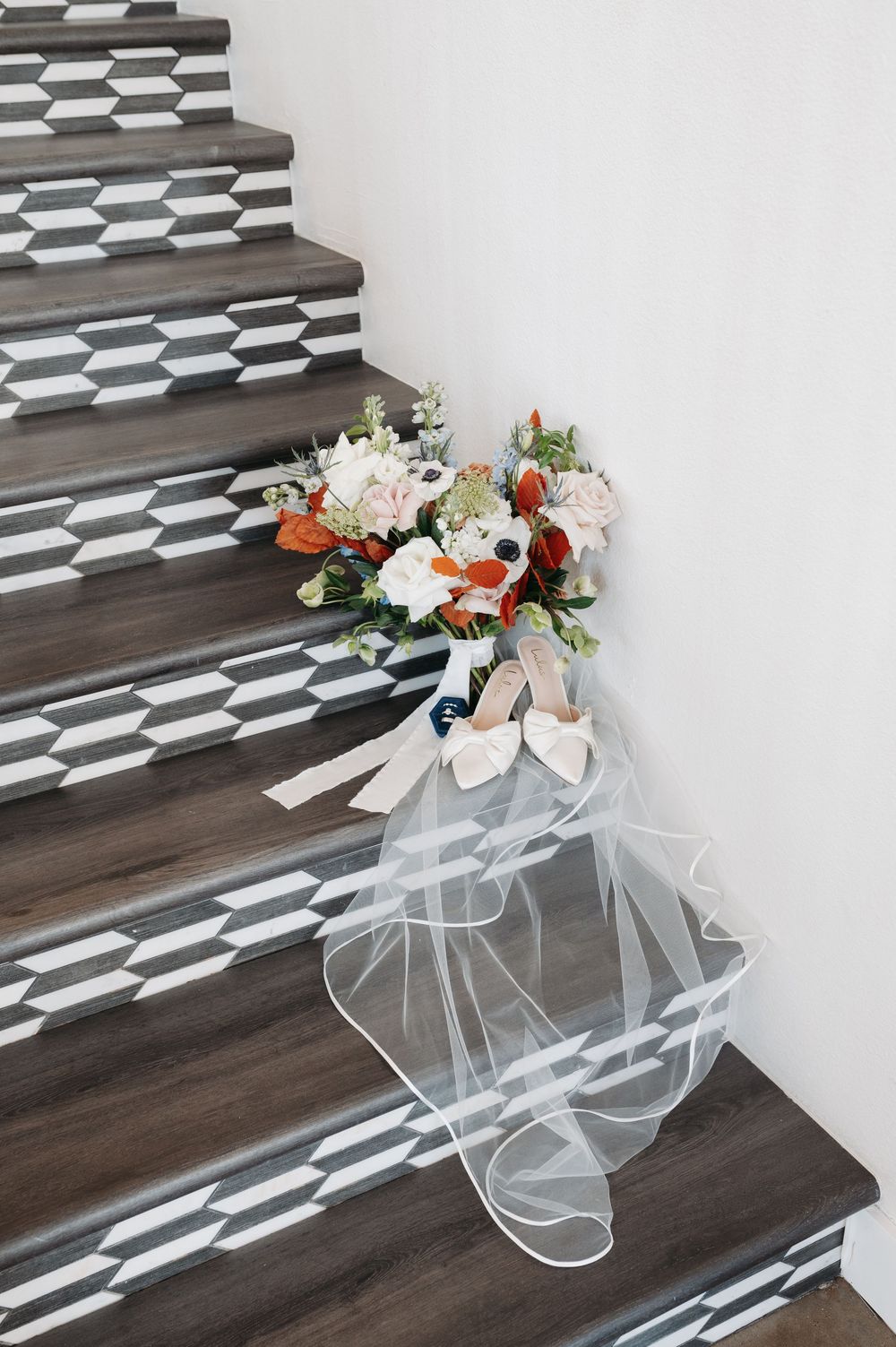 Bridal bouquet with white and orange flowers resting on geometric patterned staircase steps with a flowing veil.