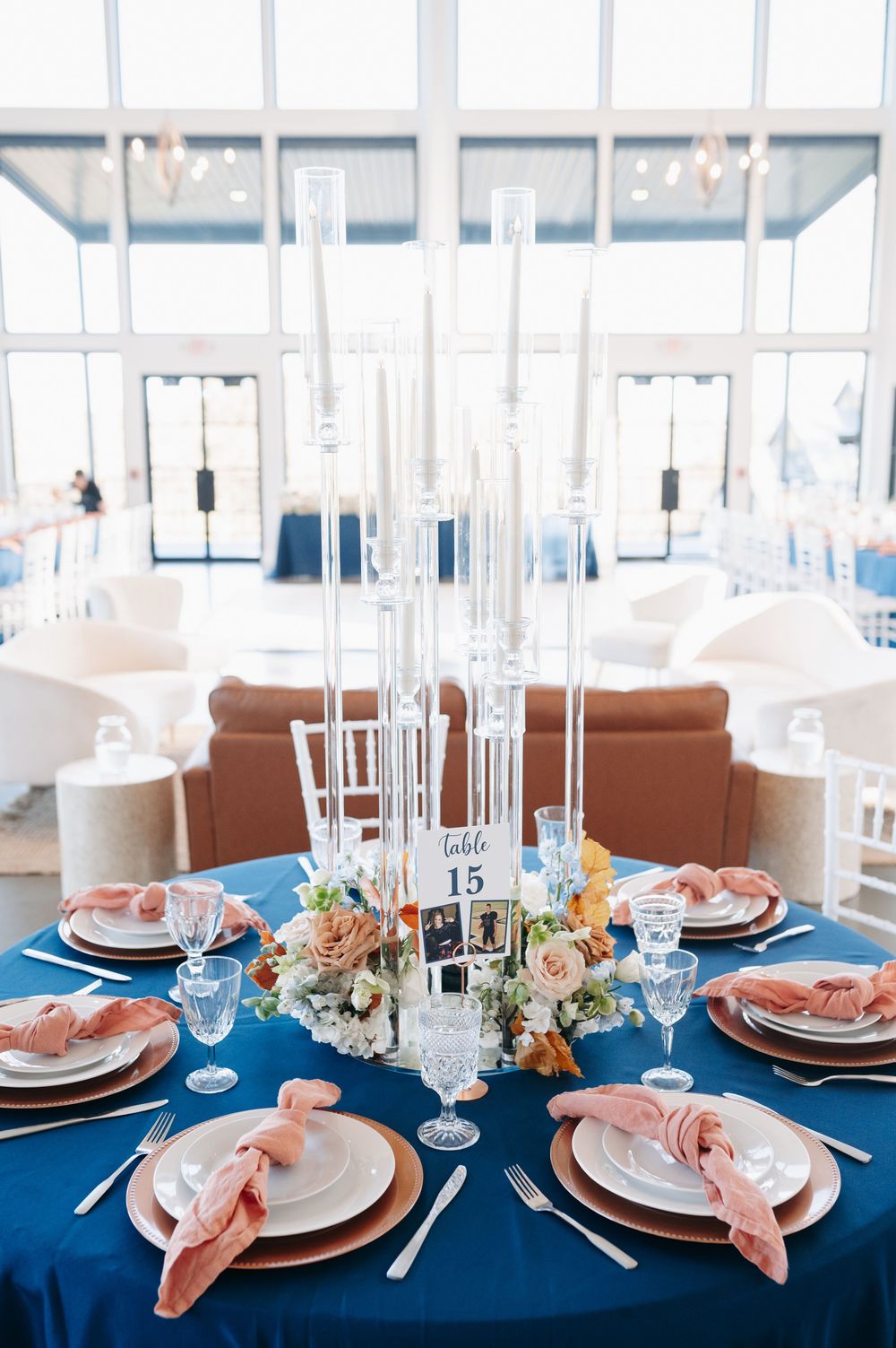Navy blue wedding table with tall crystal candelabra centerpiece, blush napkins, gold chargers, and table number 15.