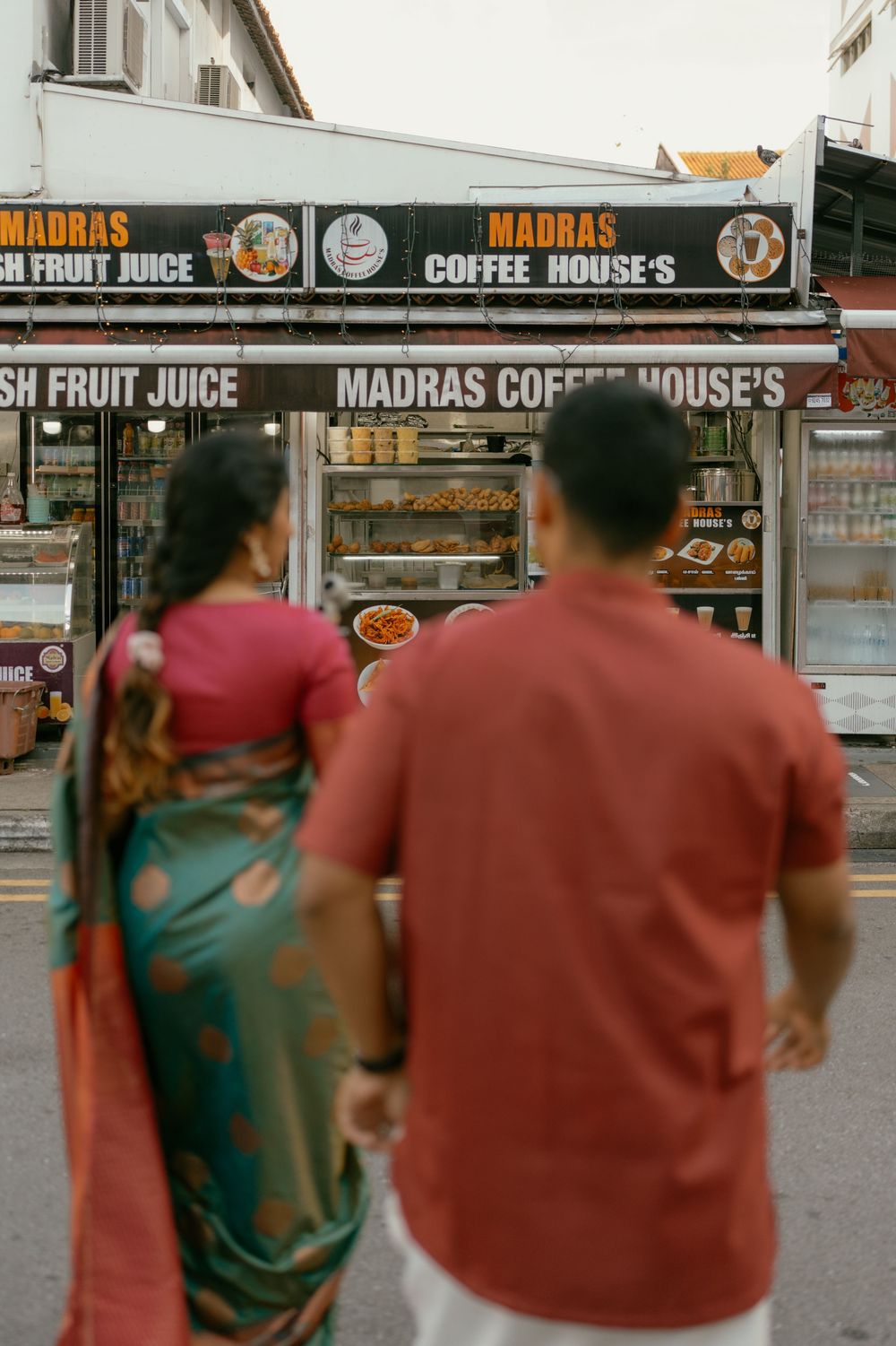 Couple in traditional Indian attire walking toward Madras Coffee House street food stall in Singapore.