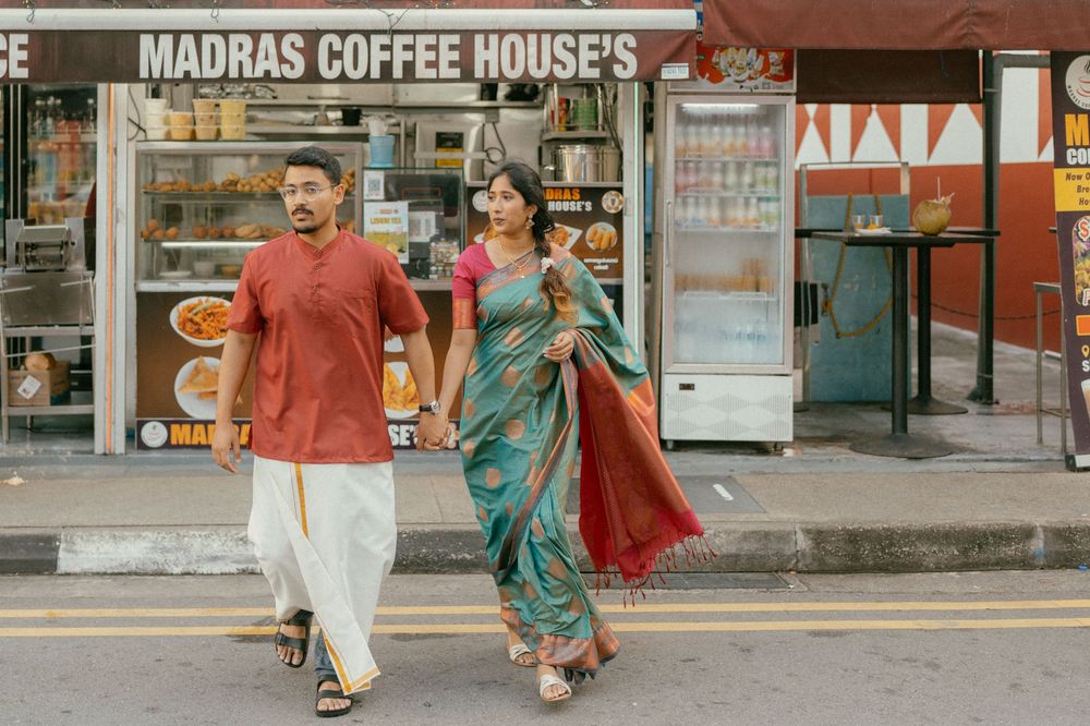A couple in traditional Indian attire walks hand-in-hand past Madras Coffee House on a busy street.