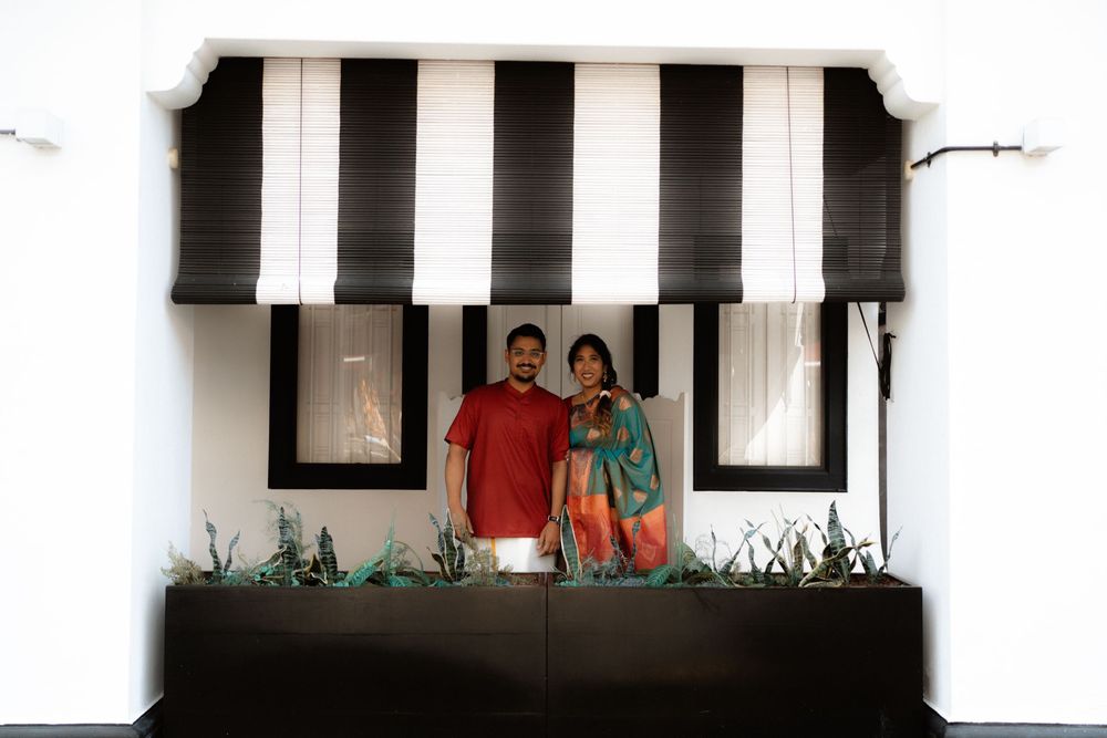 A couple smiling together under a black and white striped awning with a decorative planter box.