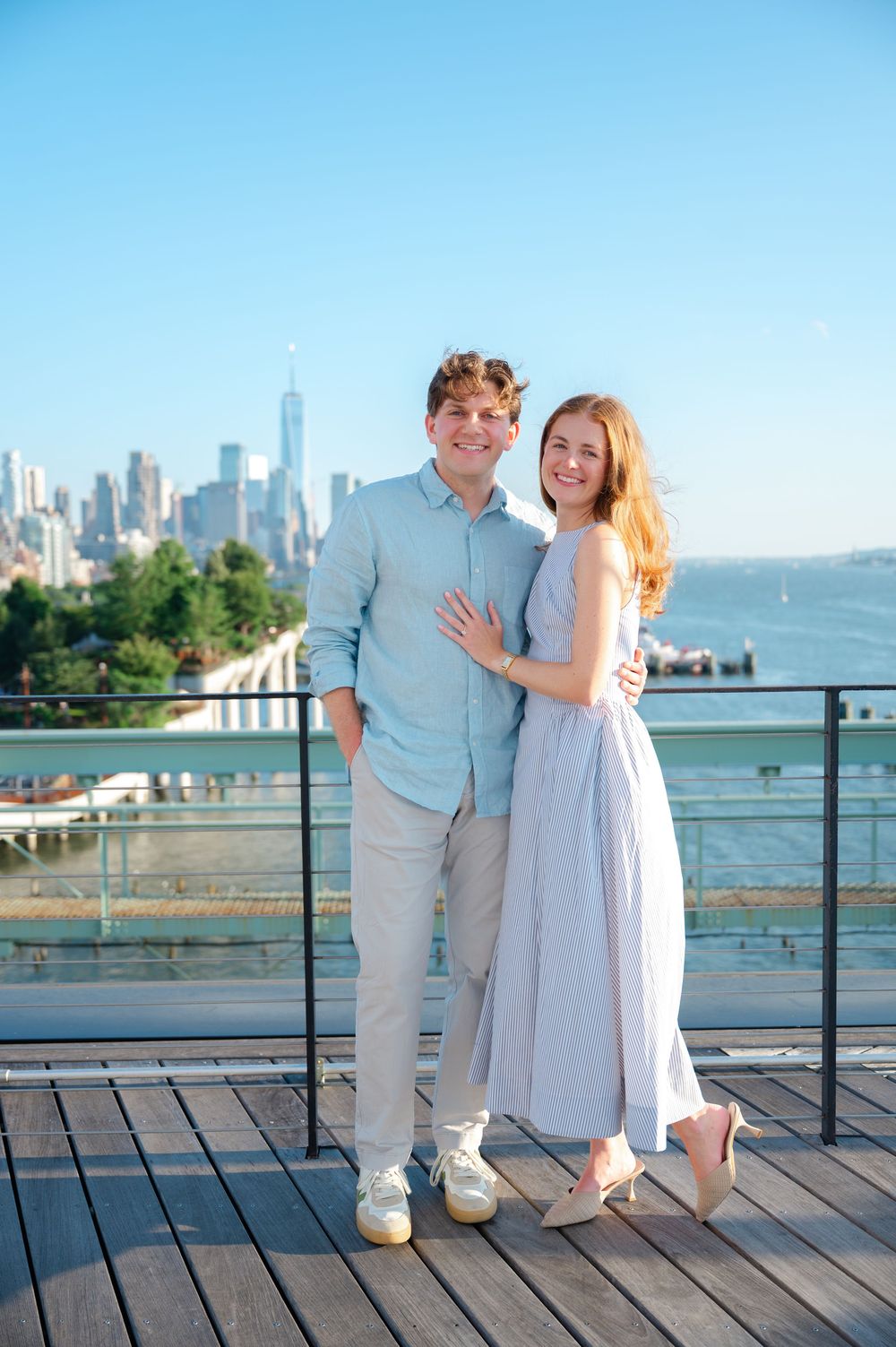 Happy engaged couple posing together on rooftop with NYC skyline and Hudson River.