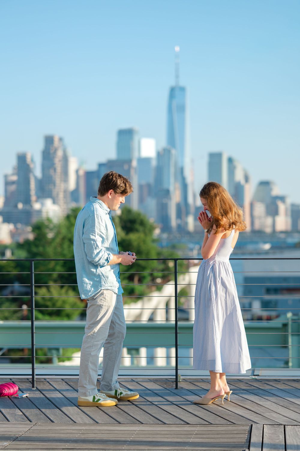 Couple sharing a marriage proposal moment on a rooftop deck with NYC skyline and One World Trade Center in background.