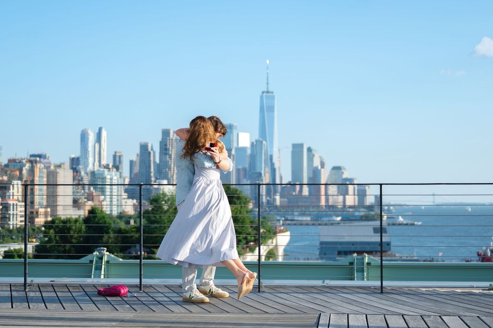 Couple embracing on rooftop terrace with stunning New York City skyline and One World Trade Center in background.