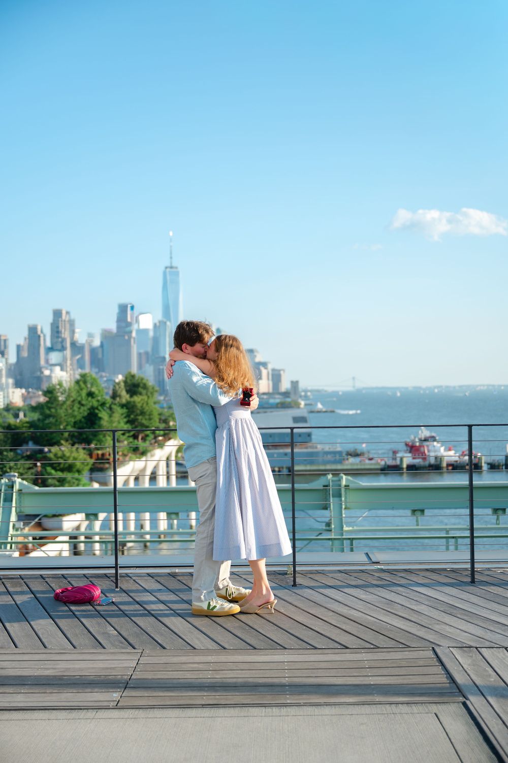 Couple kissing on a rooftop deck with NYC skyline and Hudson River in the background on a sunny day.