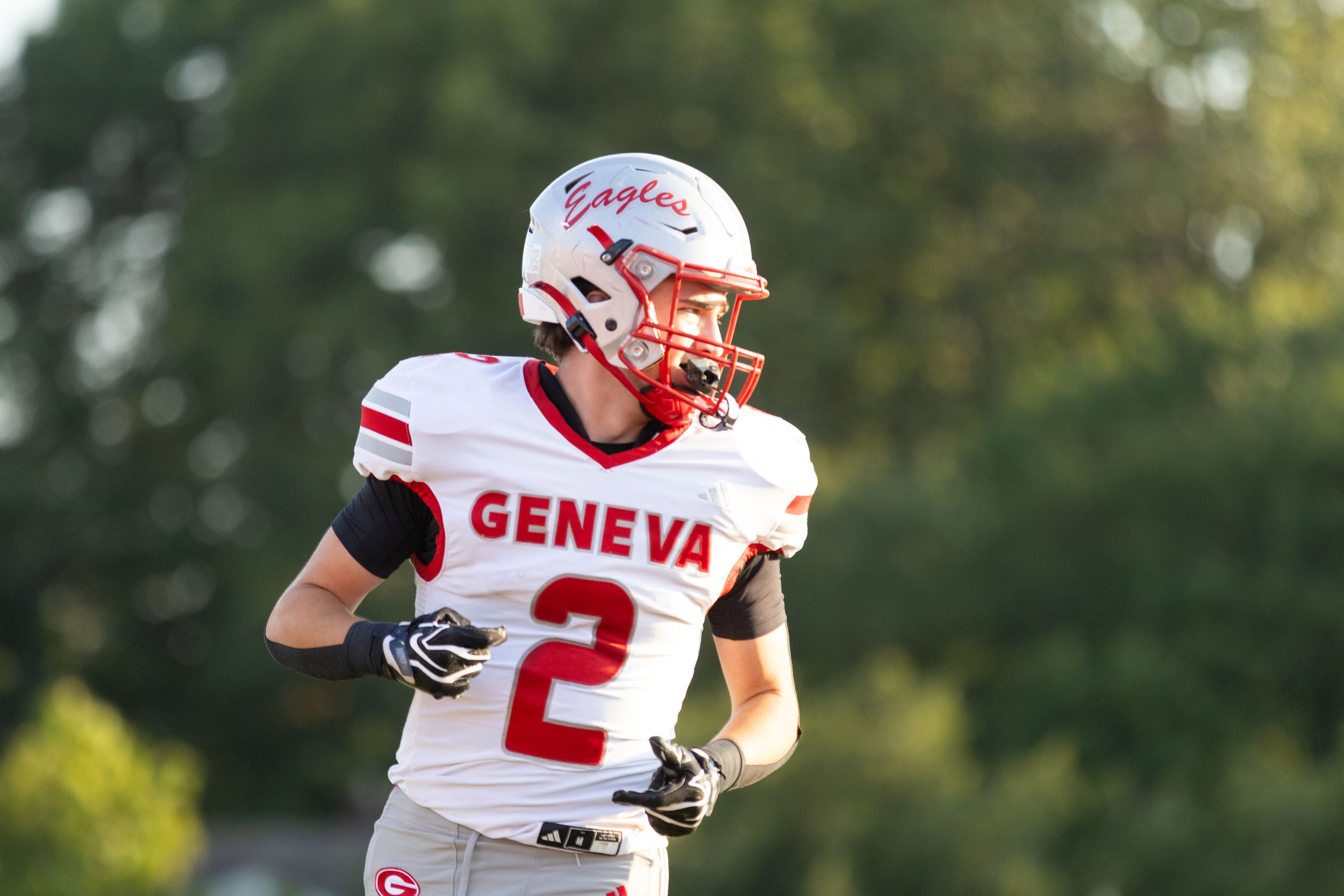 Geneva Eagles football player #2 in white uniform and red helmet jogging on field during a game.