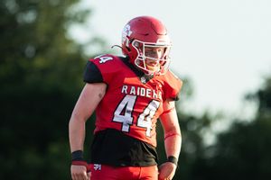 Football player wearing red Raiders jersey number 44 stands on field during game.