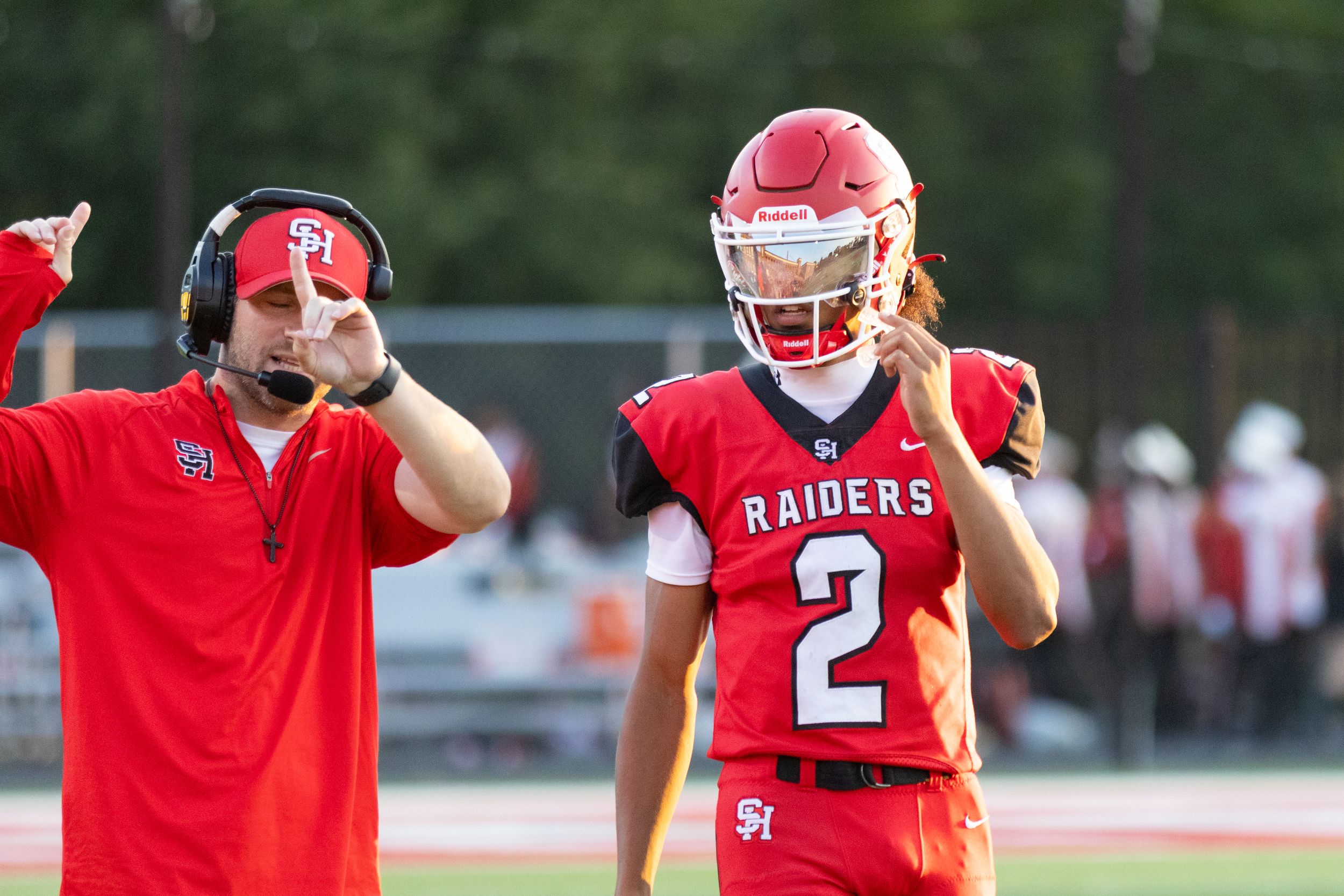 Raiders football player #2 consults with coach on sideline during a competitive high school football game.