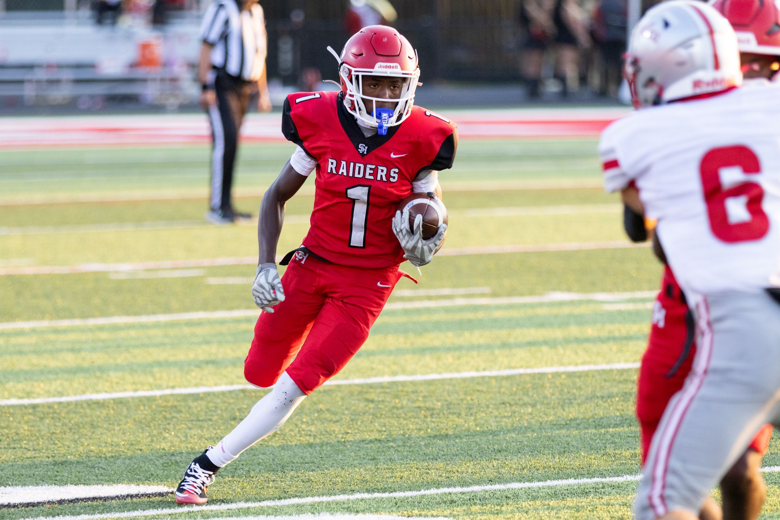 Raiders football player #1 in red uniform runs with the ball during a competitive high school football game.