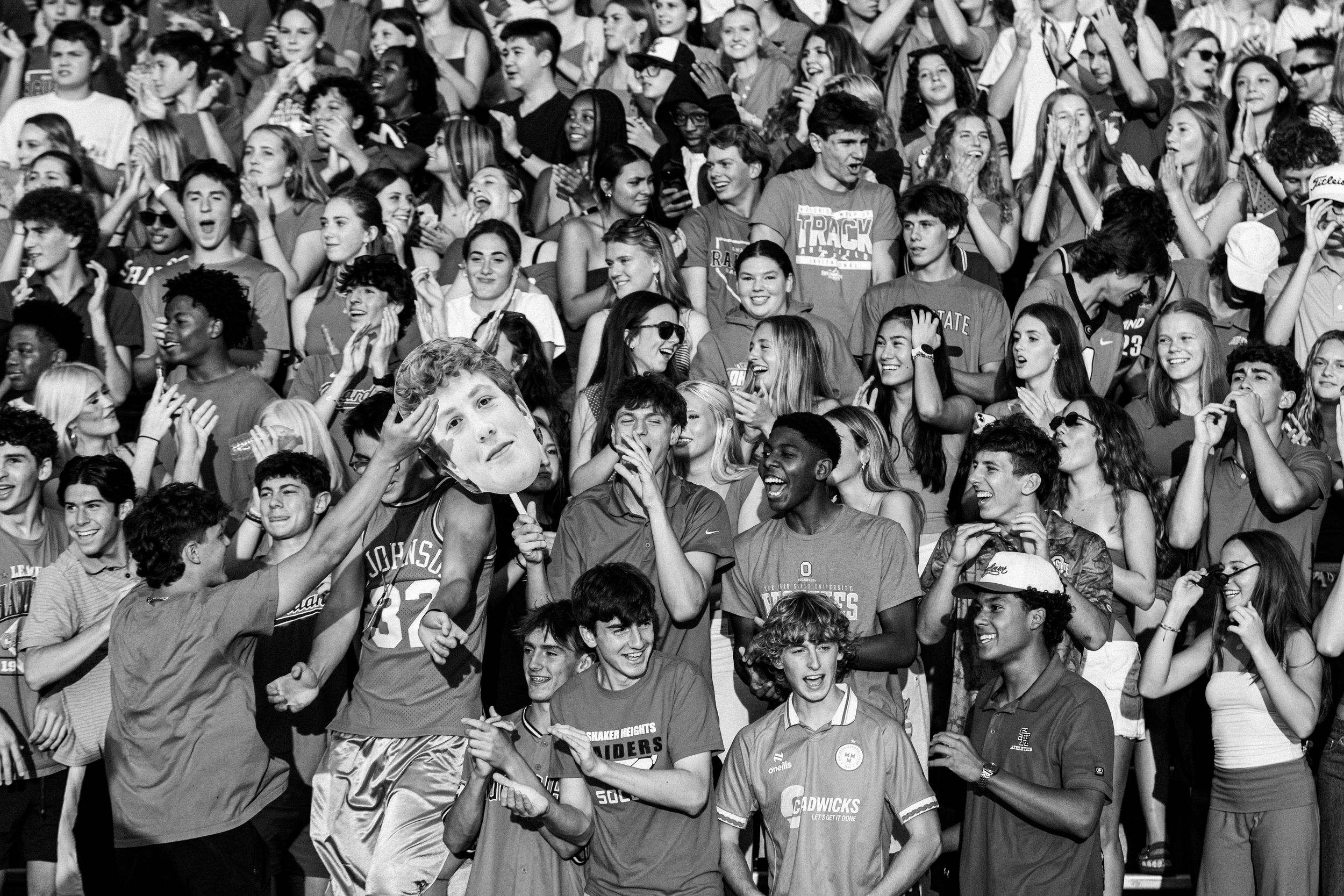 Black and white photo of a large crowd of enthusiastic students cheering at a school sports event.