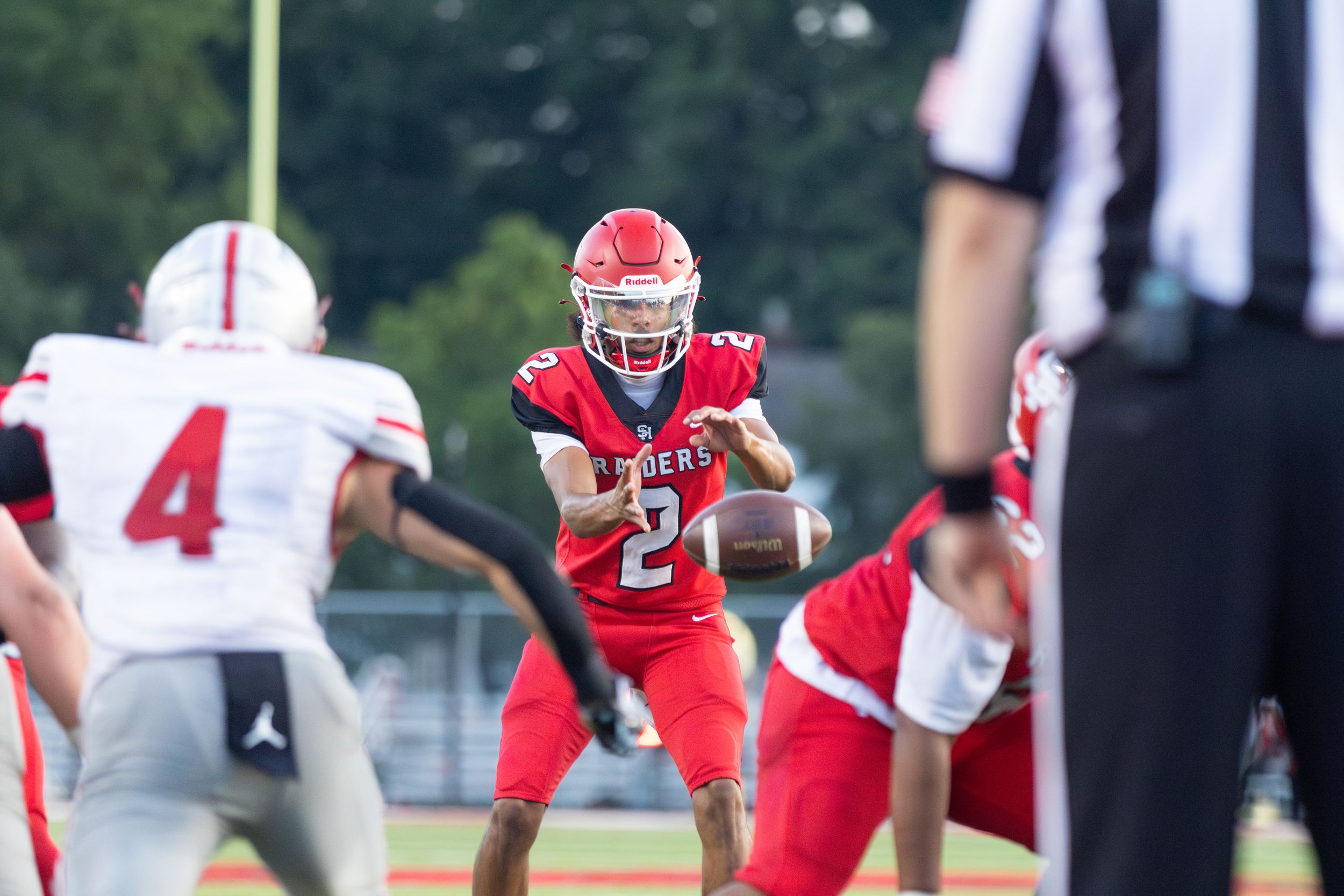 High school football player in red uniform number 21 prepares to throw pass during outdoor game.