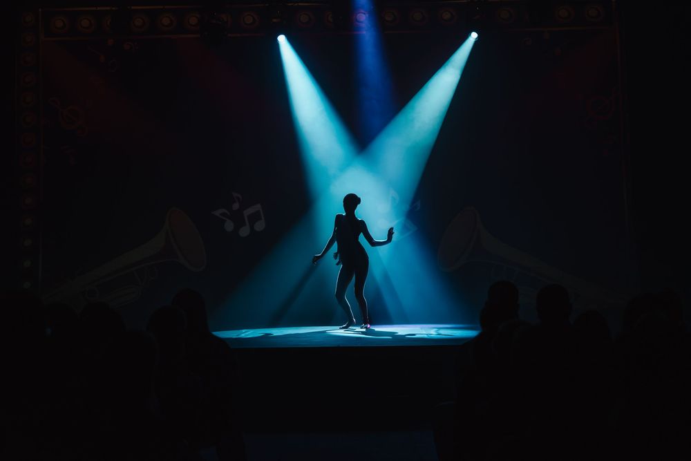 Silhouette of a performer on stage under blue spotlights in a dark theater.