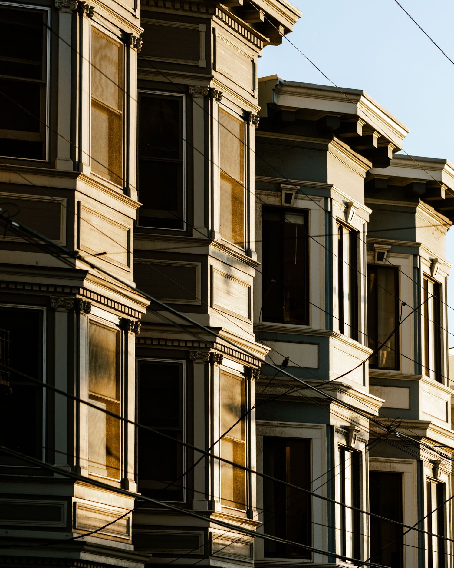 Golden sunlight reflects off ornate Victorian apartment building facades with bay windows in San Francisco.