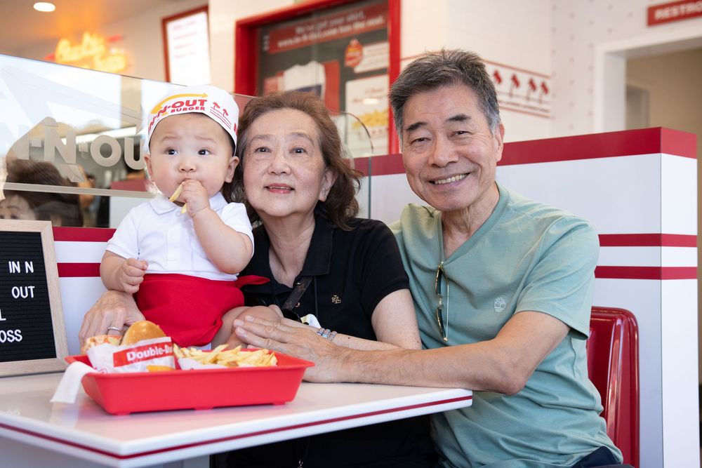 Grandparents and baby enjoy a meal at In-N-Out Burger, smiling together at a red booth.