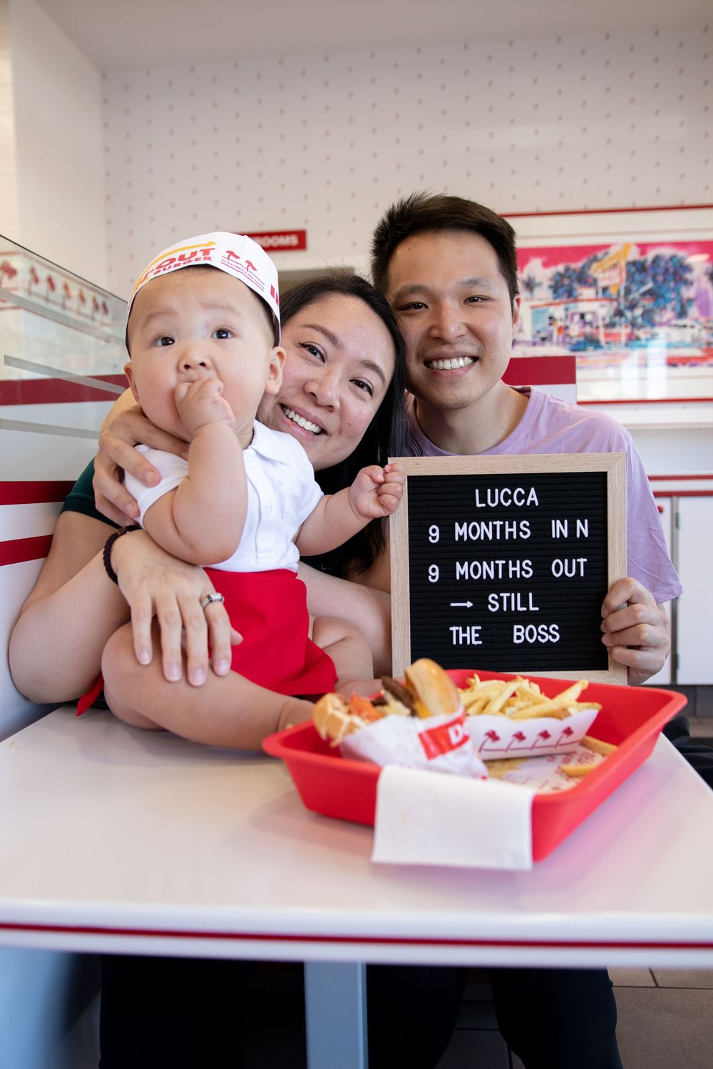 Family celebrating baby Lucca's 9-month milestone at In-N-Out Burger, holding a letter board sign.
