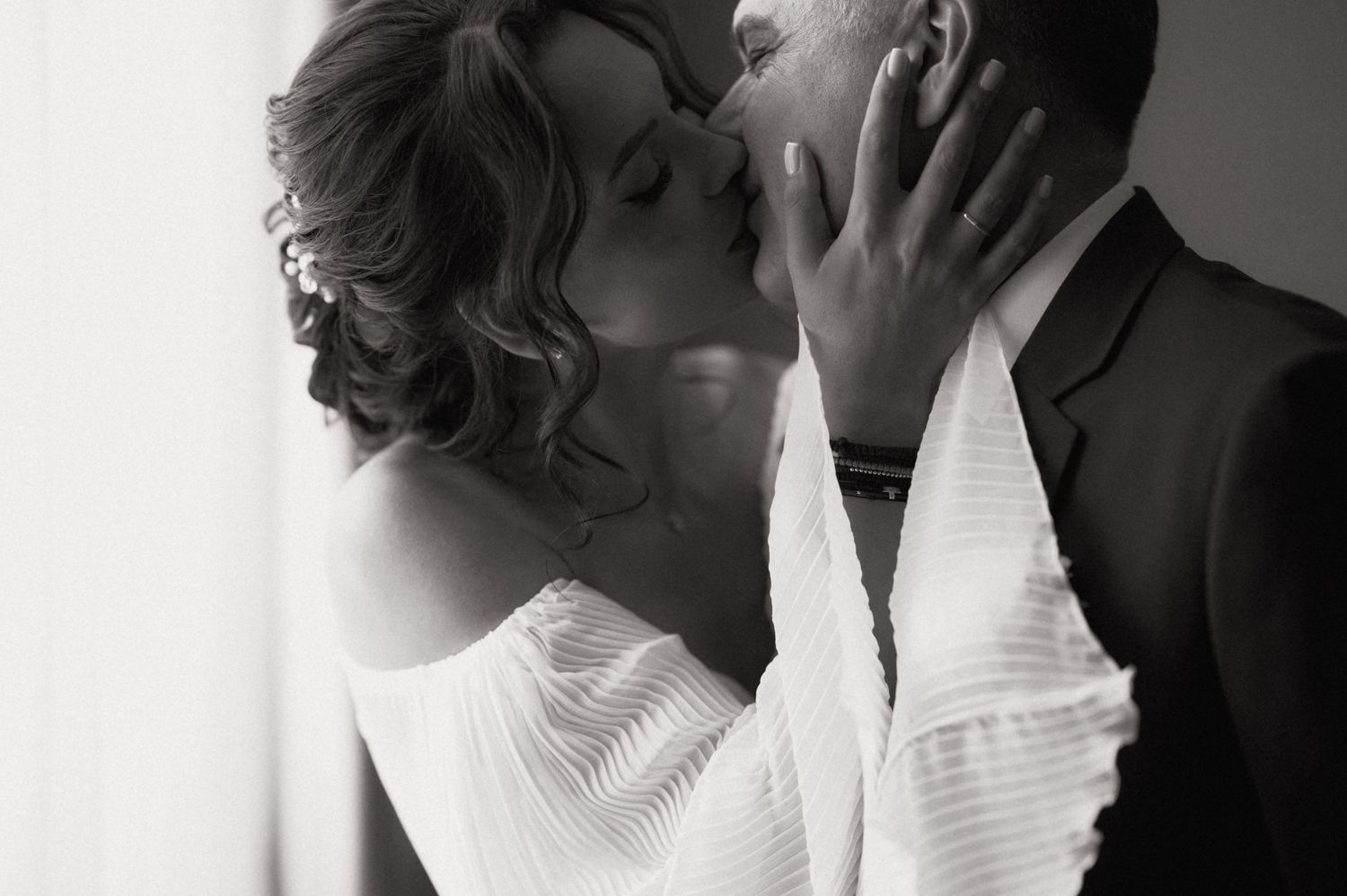Black and white photo of a couple sharing a romantic kiss, bride in white dress and groom in dark suit.