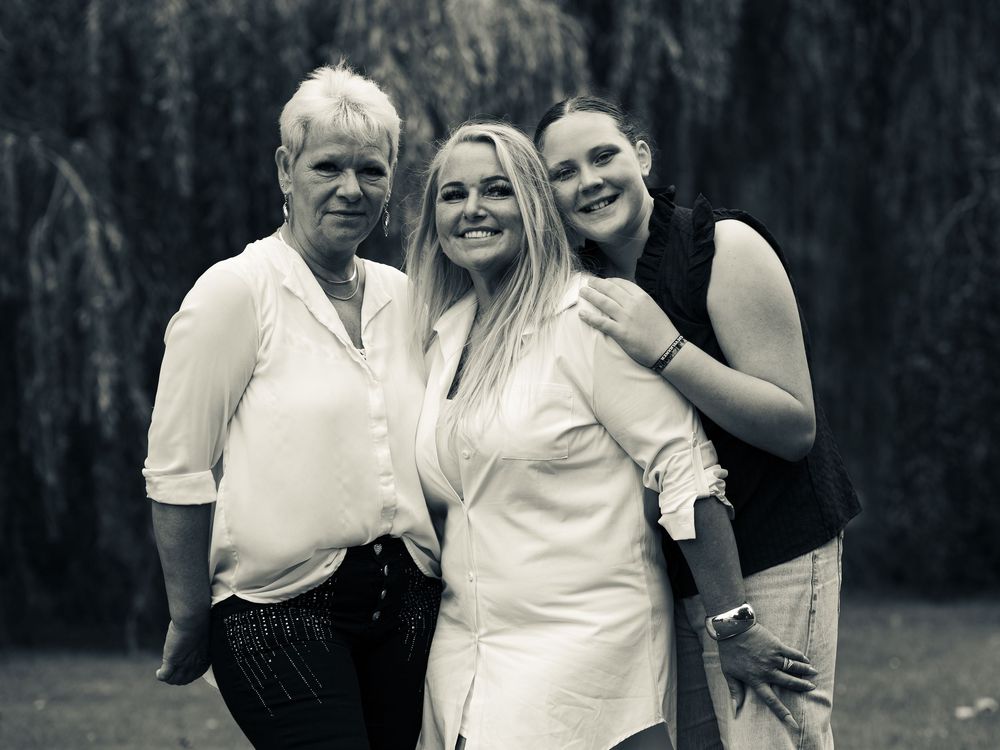 Black and white photo of three smiling women posing together outdoors near a weeping willow tree.