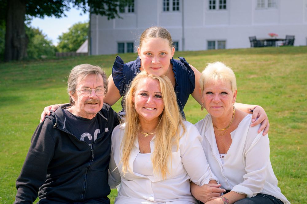 Happy family of four smiling together on green grass outdoors on a sunny day.