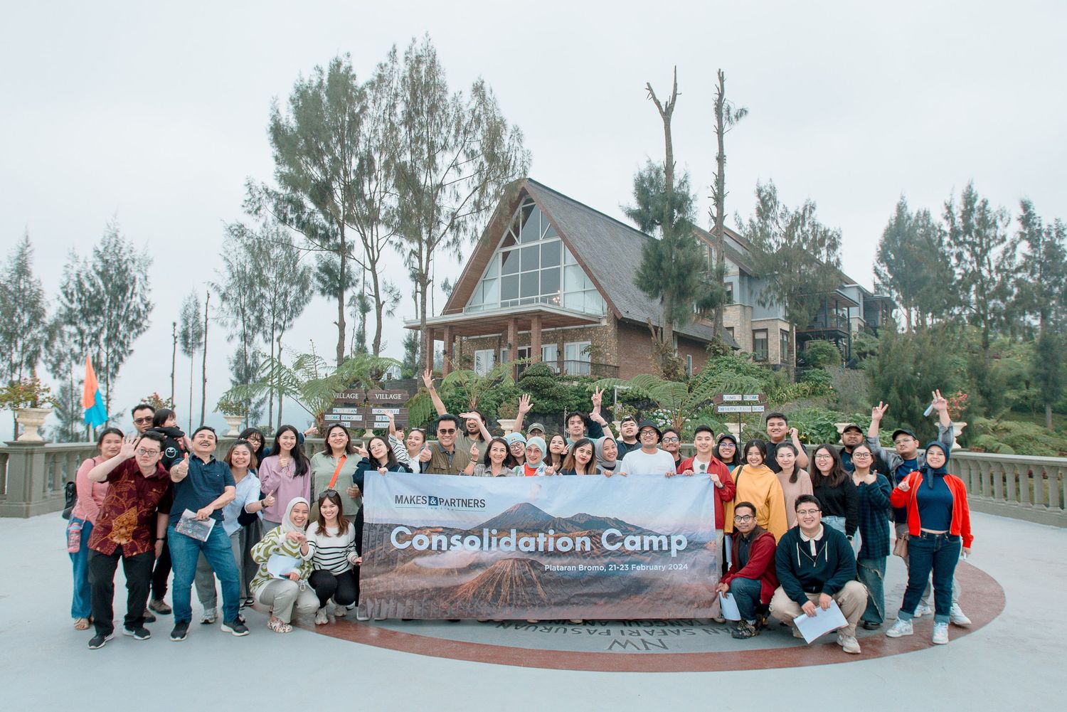 Large group of people posing outdoors at a Consolidation Camp event near a scenic chalet building.