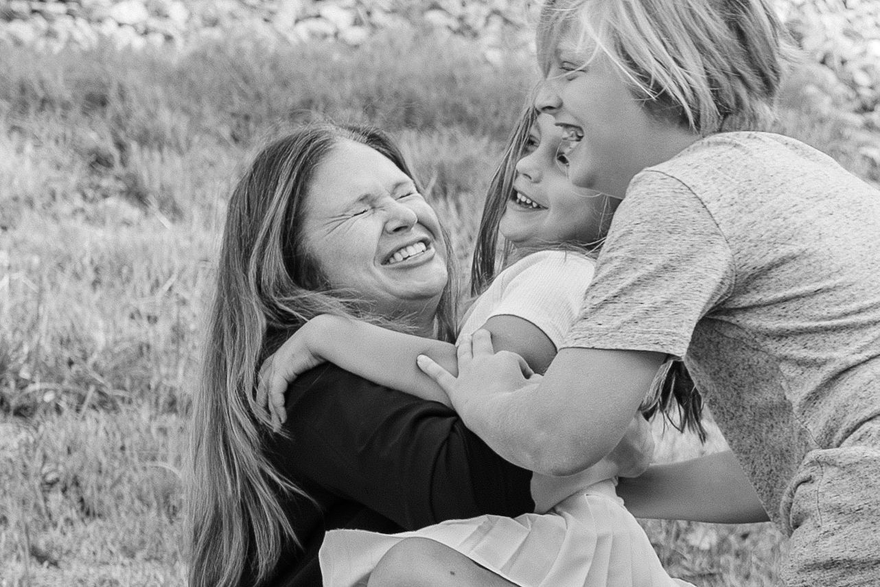 Black and white photo of three women laughing and hugging outdoors in a joyful family embrace.
