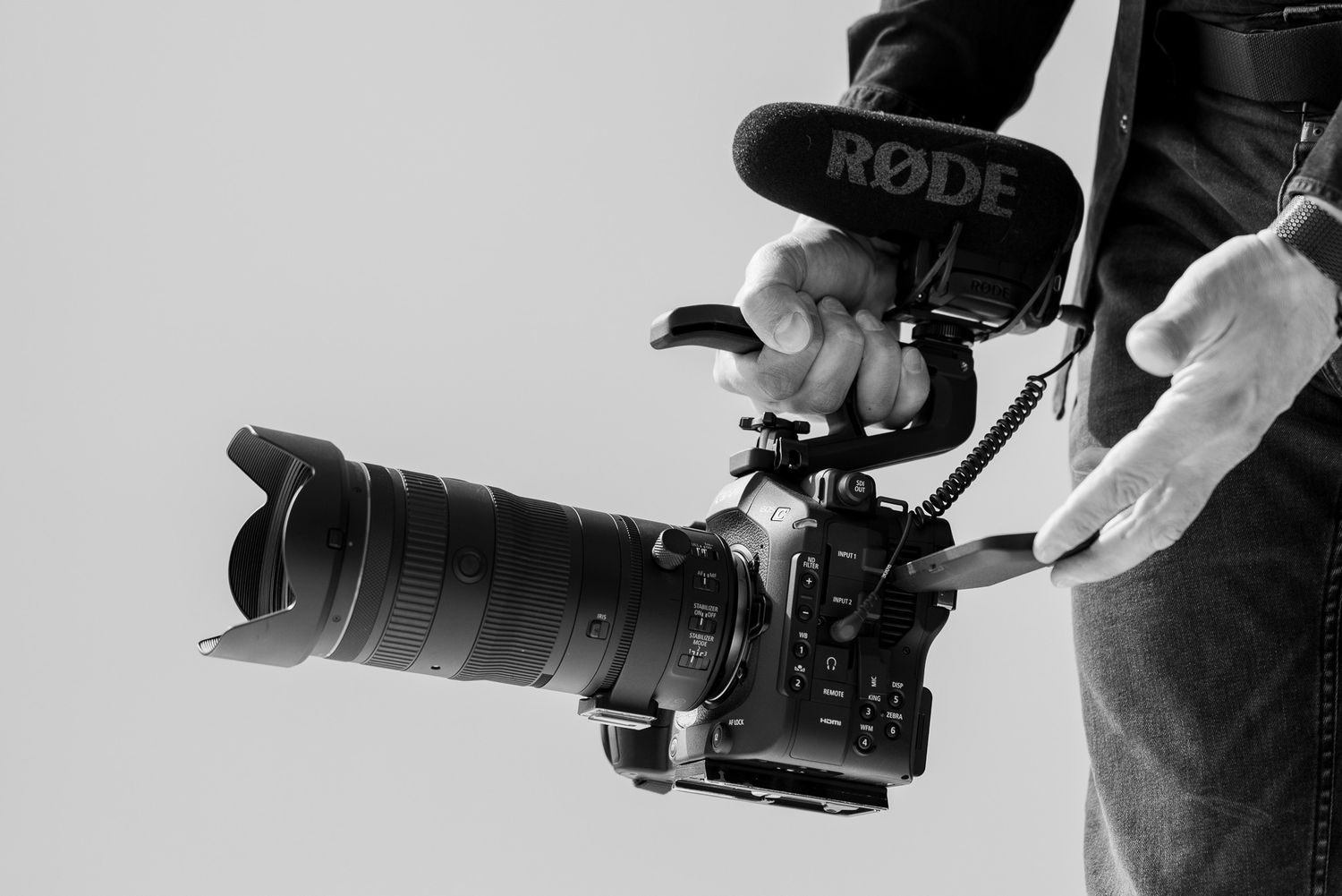 Black and white photo of a person holding a professional camera rig with a Rode microphone attached.