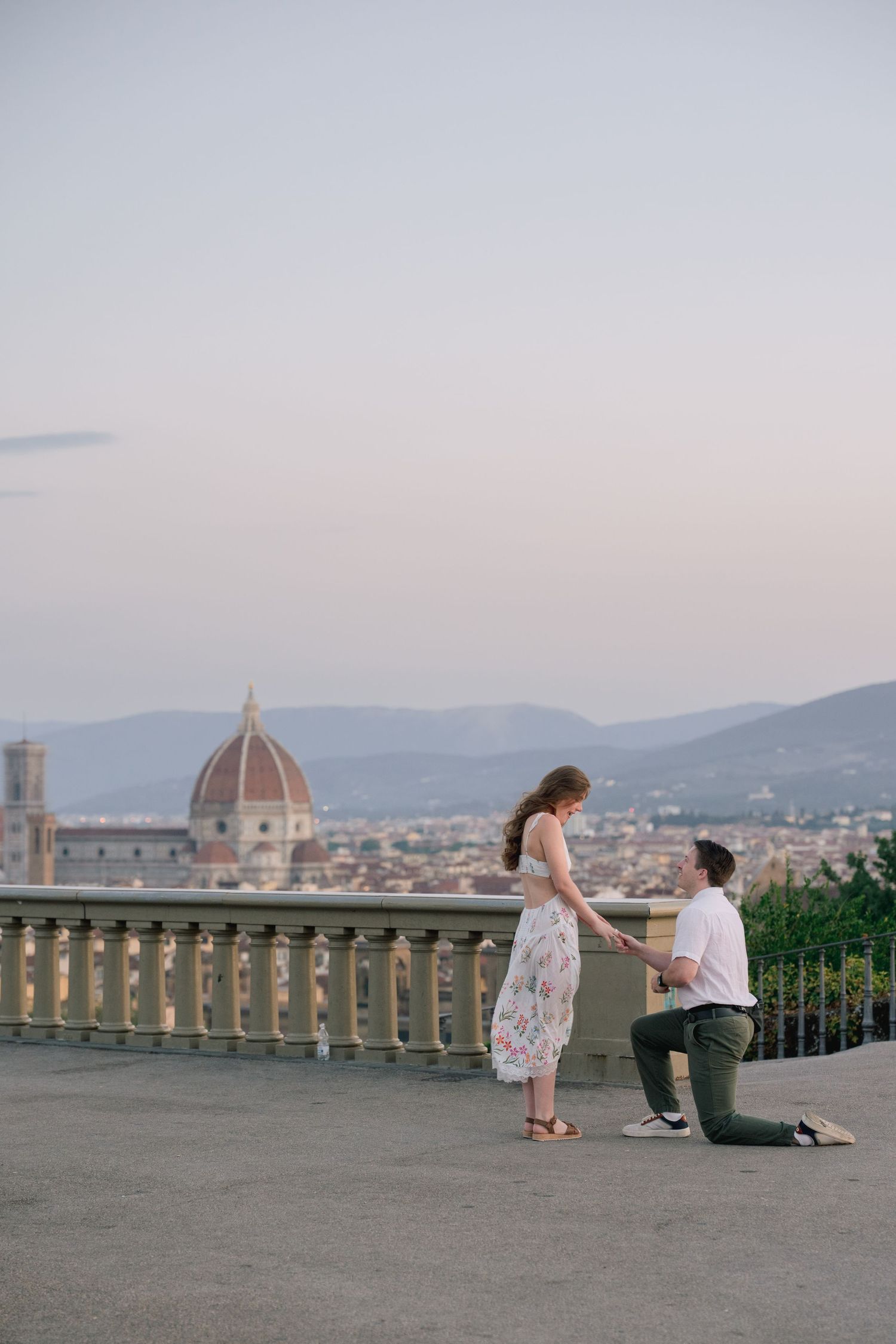 Man proposing on one knee to woman on scenic Florence terrace with Cathedral dome backdrop at dusk.