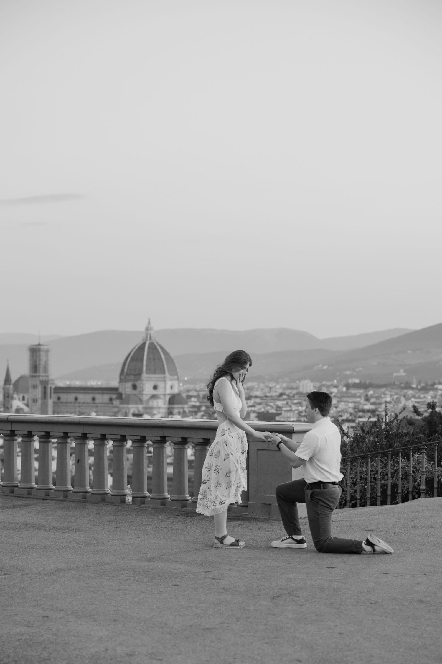 Black and white photo of a man proposing on one knee to a woman with Florence cathedral skyline backdrop.