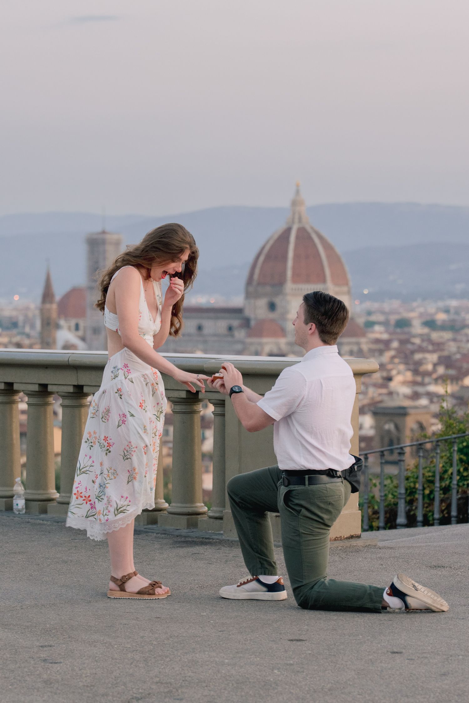 Man proposes on one knee to woman at Piazzale Michelangelo with Florence skyline and Duomo backdrop.